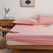Hands stretch the elasticated corner of the Sola Cotton Fitted Sheet in Blush over a mattress