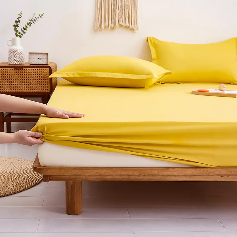 Hands pull the elasticated corner of the Sola Cotton Fitted Sheet in Butter over a mattress