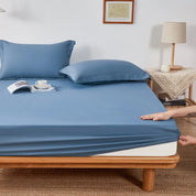 Sola Cotton Fitted Sheet in slate blue, hand pulling elasticated corner snug over mattress