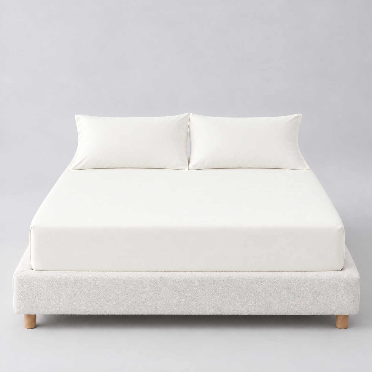 Sola Cotton Fitted Sheet in Ivory, fitted on a mattress with matching pillowcases against a boucle bed base