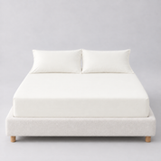 Sola Cotton Fitted Sheet in Ivory, fitted on a mattress with matching pillowcases against a boucle bed base