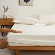 Hands fitting the Sola Cotton Fitted Sheet in Ivory over a mattress corner on a wooden bed frame
