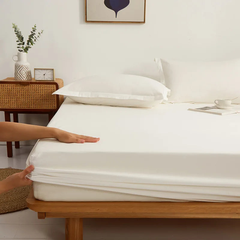Hands fitting the Sola Cotton Fitted Sheet in Ivory over a mattress corner on a wooden bed frame