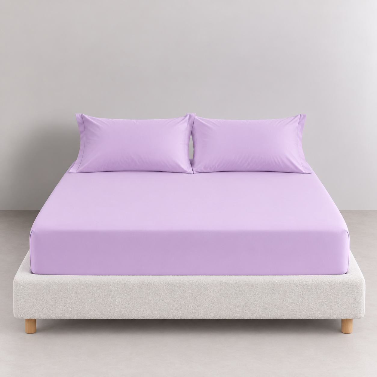 Sola Cotton Fitted Sheet in Lilac fitted snugly on a bed with matching pillowcases, upholstered base