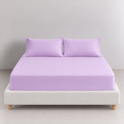 Sola Cotton Fitted Sheet in Lilac fitted snugly on a bed with matching pillowcases, upholstered base