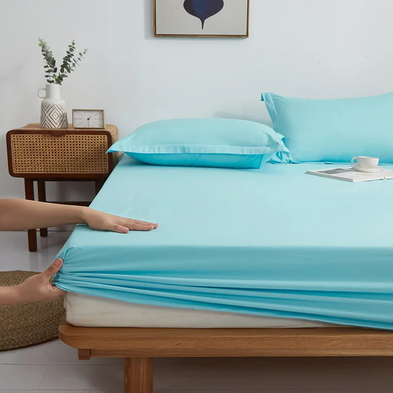 Hands pull the elasticated corner of the Sola Cotton Fitted Sheet in Sky over a mattress edge