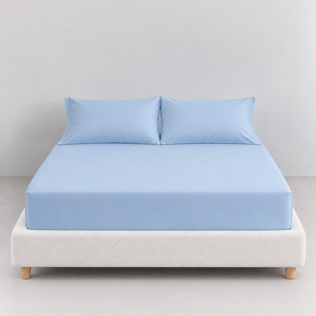 Sola Cotton Fitted Sheet in Sky, soft blue cotton fitted to a bed with matching pillowcases on a boucle base