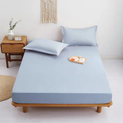 Sola Cotton Fitted Sheet in Sky, styled on a bed with matching pillowcases beside a rattan side table