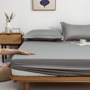 Hands tuck the elasticated corner of the Sola Cotton Fitted Sheet in grey over a mattress