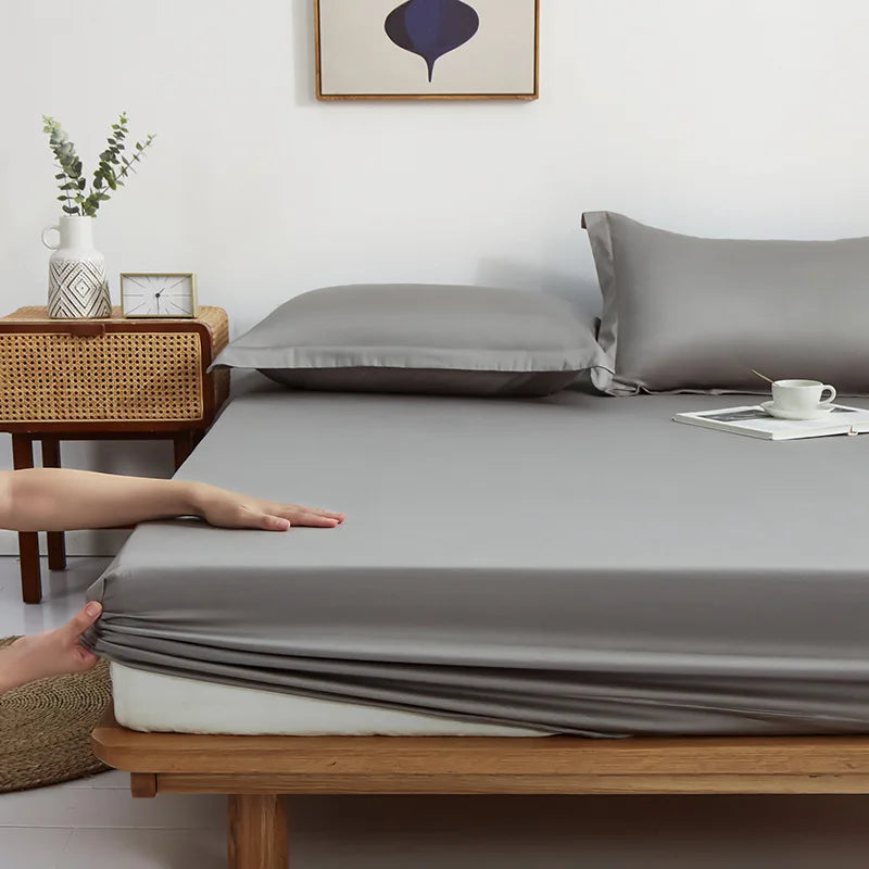 Hands tuck the elasticated corner of the Sola Cotton Fitted Sheet in grey over a mattress