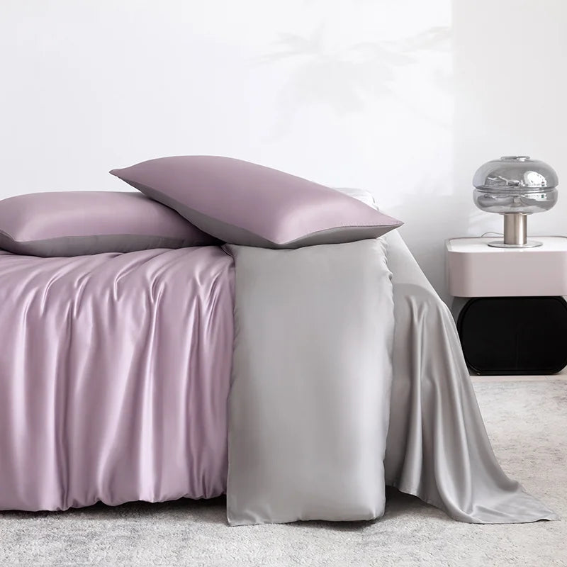 Soléa Bamboo Bedding Set in Charm Purple - Grey, sateen sheets draped over a bed beside a nightstand lamp