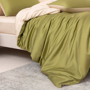 Soléa Bamboo Bedding Set in olive green sateen with beige reverse, draped loosely over a bed corner