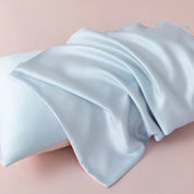 Close-up of pale blue sateen fabric from the Soléa Bamboo Bedding Set draped over a pink-trimmed pillow