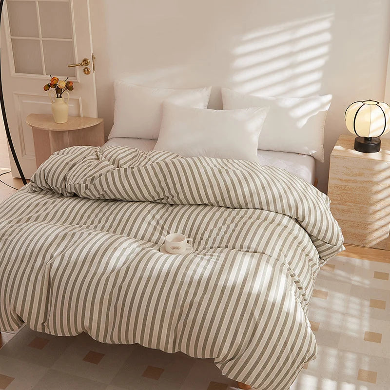 Soleil Stripe Bedding Set in Ivory Taupe, sunlit bed with rumpled quilt and white pillows, mug resting on top