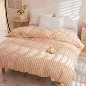 Soleil Stripe Bedding Set in peach and white stripes on a made bed, sunlit bedroom with a cup on top