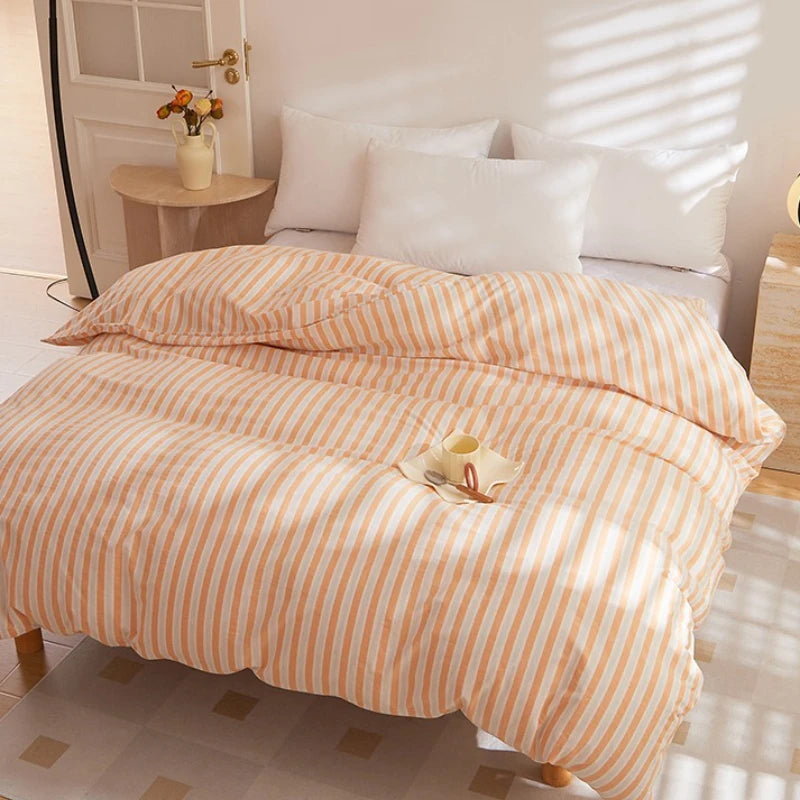 Soleil Stripe Bedding Set in peach and white stripes on a made bed, sunlit bedroom with a cup on top