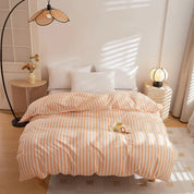 Soleil Stripe Bedding Set in peach and white stripes, made bed with white pillows in a sunlit room