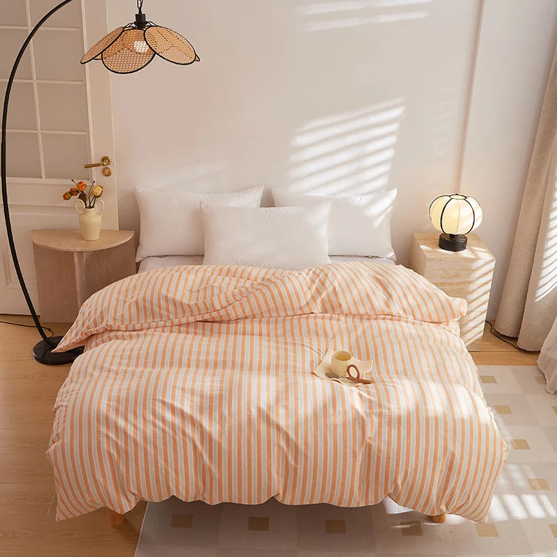 Soleil Stripe Bedding Set in peach and white stripes, made bed with white pillows in a sunlit room