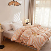 Soleil Stripe Bedding Set in soft peach and white stripes, styled on a bed by a sunlit window