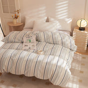 Soleil Stripe Bedding Set in cream with blue and orange stripes, made up on a sunlit bed with a newspaper