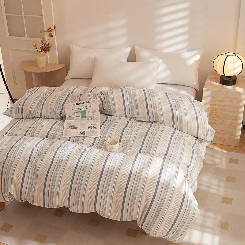 Soleil Stripe Bedding Set in cream with blue and orange stripes, made up on a sunlit bed with a newspaper