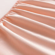 Close-up of the Tate Fitted Sheet's elasticised edge gathered on soft pink fabric, showing smooth twill weave