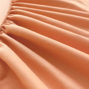 Close-up of the Tate Fitted Sheet in Orange, showing the elasticised edge and smooth twill weave