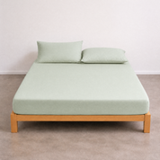 Tate Fitted Sheet in sage green on a timber bed frame, with two matching pillows against a plain wall