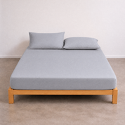 Tate Fitted Sheet in soft grey on a wooden bed frame, with matching pillowcases against a plain wall
