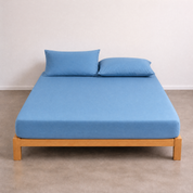 Tate Fitted Sheet in soft blue on a wooden bed frame, with matching pillowcases, styled against a plain wall