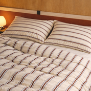 Vida Bedding Set styled on a bed, cream with rust and blue stripes, warm lamplit bedroom setting