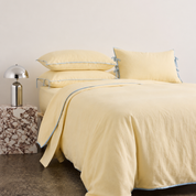 Wren Bedding Set in Buttermilk, made bed with pale blue trim edging and tied pillowcase corners