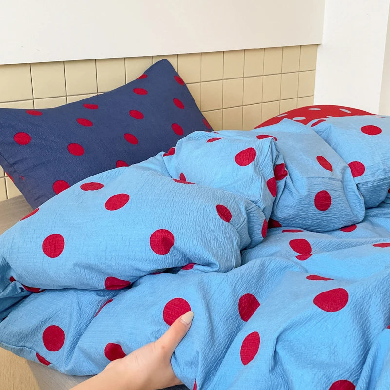 A hand touches the crinkled cotton of the Ziggy Spot Bedding Set, cherry dots on soft blue and navy