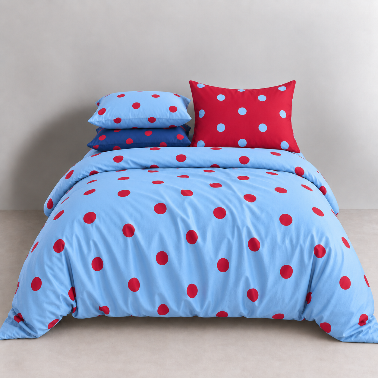 Ziggy Spot Bedding Set styled on a bed, cherry red spots on a soft blue quilt cover with matching pillowcases