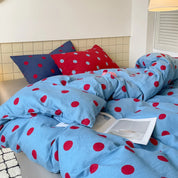 Ziggy Spot Bedding Set rumpled on a bed, cherry-red spots on blue cotton, navy and red spot cushions behind