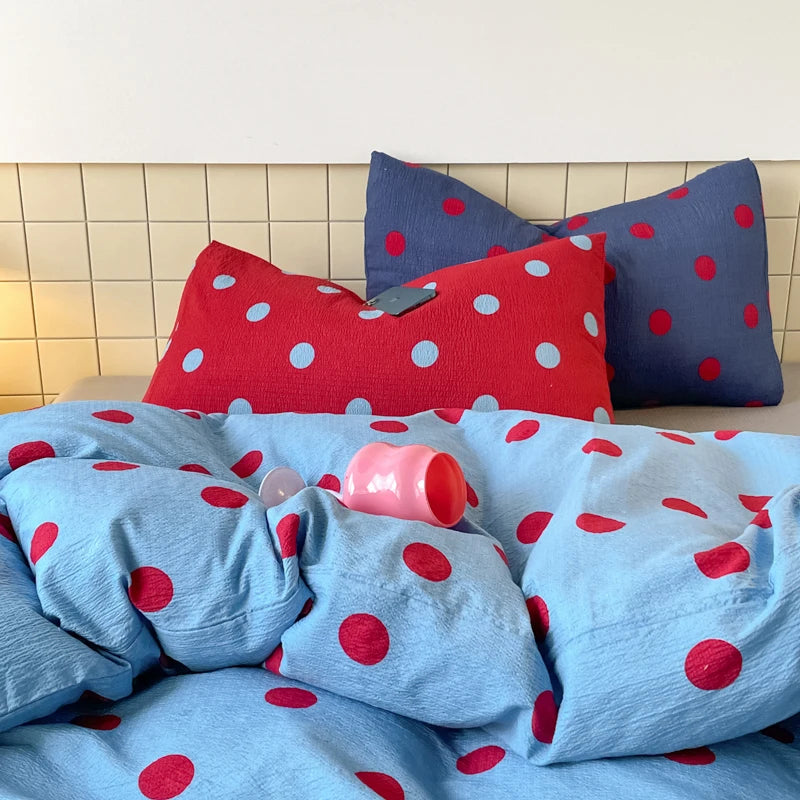 Ziggy Spot Bedding Set rumpled on a bed, cherry-red spots on blue cotton with red and navy pillowcases behind