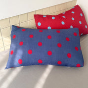 Ziggy Spot Bedding Set pillowcases in blue with red spots, and red with blue spots, propped on a bed