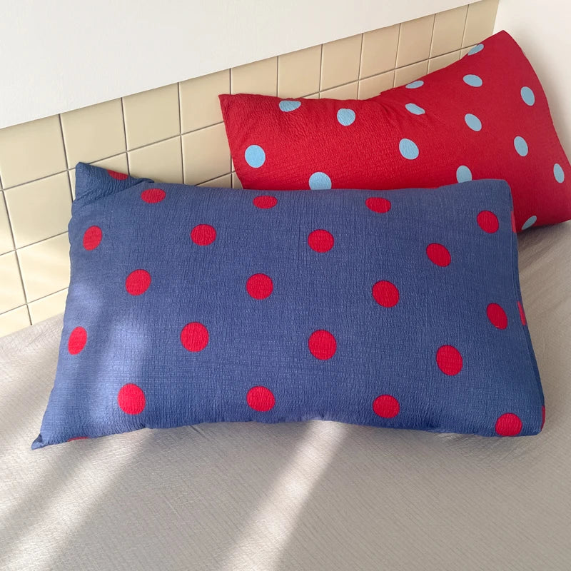 Ziggy Spot Bedding Set pillowcases in blue with red spots, and red with blue spots, propped on a bed