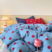 Ziggy Spot Bedding Set rumpled on a bed, sky blue with cherry red spots, mixed navy and red pillowcases behind